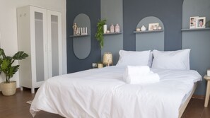 A neatly made bed with white linens, a bedside table with a lamp, and a wardrobe.