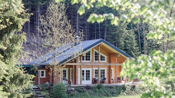 Eine Blockhütte mit einer großen Veranda, umgeben von einem Wald.