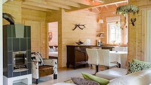 Ein gemütliches Blockhaus mit Kamin, Holzwänden, einer Essecke und einem Wohnbereich mit Sofa und Sesseln.