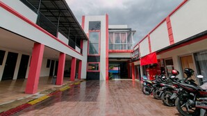 Un área interior espaciosa con piso de baldosas, paredes rojas y blancas, y una escalera central que conduce a un nivel superior. Varias motocicletas están estacionadas a la derecha.