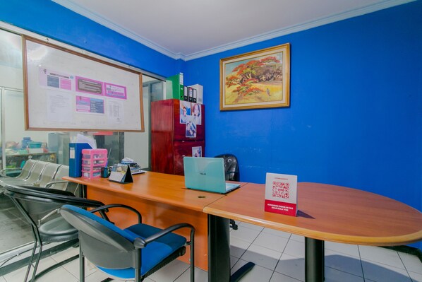 A conference room with a wooden table, blue chairs, a whiteboard, a red filing cabinet, and a framed painting on the wall.