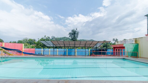 Una piscina con solárium empedrado, una zona de estar cubierta y una valla.