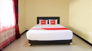 A neatly made bed with a white and red bedspread, two pillows with "OYO" branding, and a red curtain partially drawn to the side.
