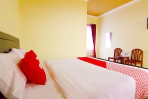 A hotel room with a bed, a red and white bedspread, a wooden headboard, a small table with chairs, and a window with curtains. - OYO 2162 Pondok Wisata Sri Widodo (Ngargoyoso)
