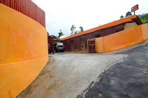 A parking area with a red car parked near a building with orange walls and a gated entrance. - OYO 2162 Pondok Wisata Sri Widodo (Ngargoyoso)