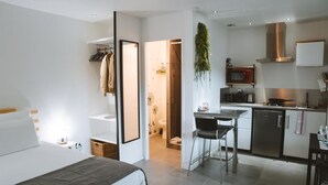 A modern hotel room with a bed, a small kitchenette, a dining area, and a bathroom. - Studio Wood Nature & Confort 3* Wifi+Parking (Laveyron)