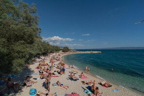 A beach with clear blue water, people sunbathing and swimming, and a line of trees on the left. - Luxury Rooms near Beach 1 (Split)