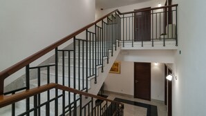 Un interior con varios niveles, una escalera de madera, barandillas negras y una puerta.
