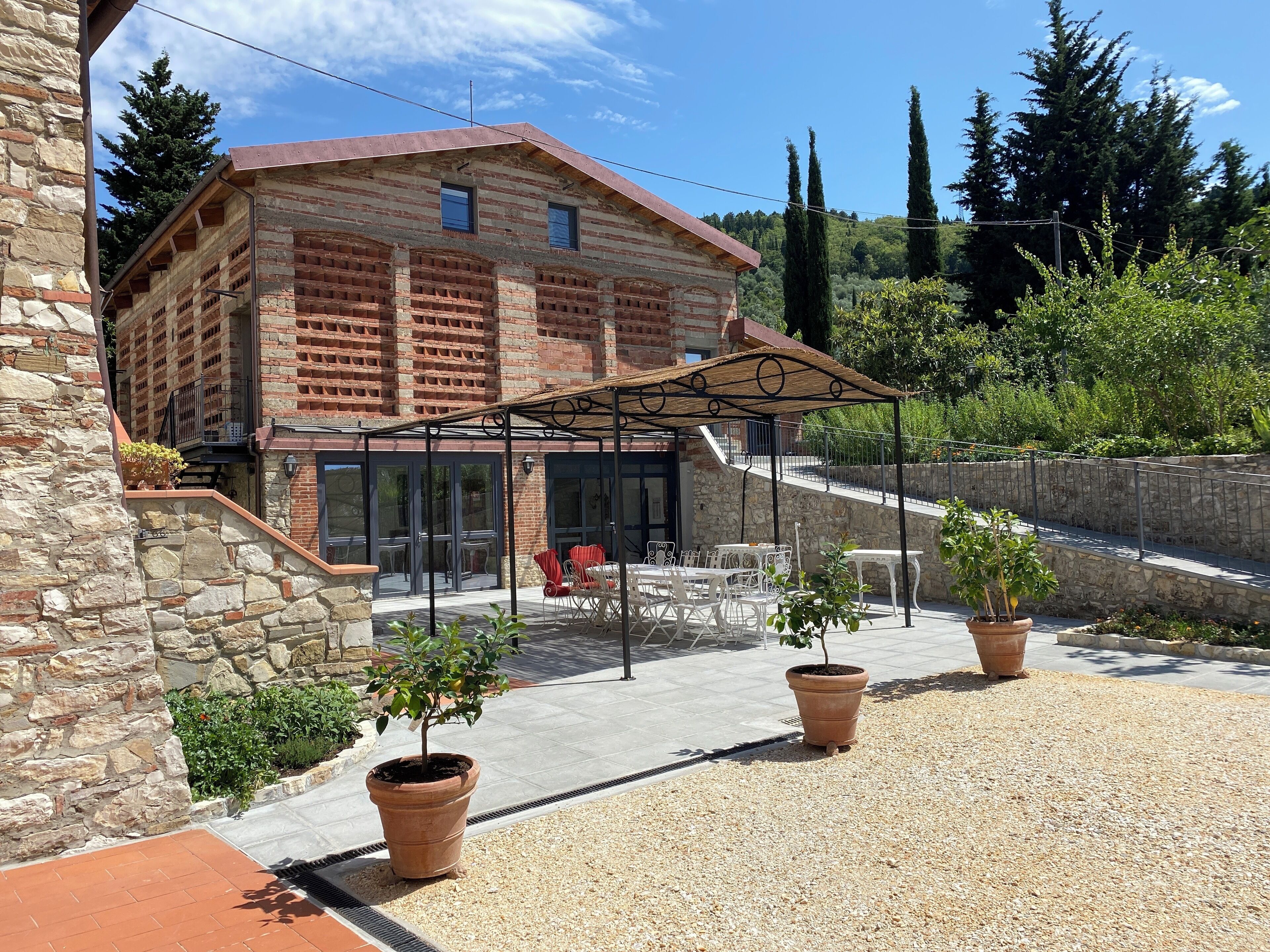 Ein Steinhaus mit Ziegelverkleidung, einer überdachten Terrasse und Gartenmöbeln, zusätzlich mit Blumentöpfen.