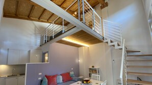 A modern kitchen with white cabinets, a dining table with chairs, a sofa with colorful cushions, and a staircase leading to an upper level. - Super-modern studio on the hills of Florence, Tuscany  (BAGNO A RIPOLI)