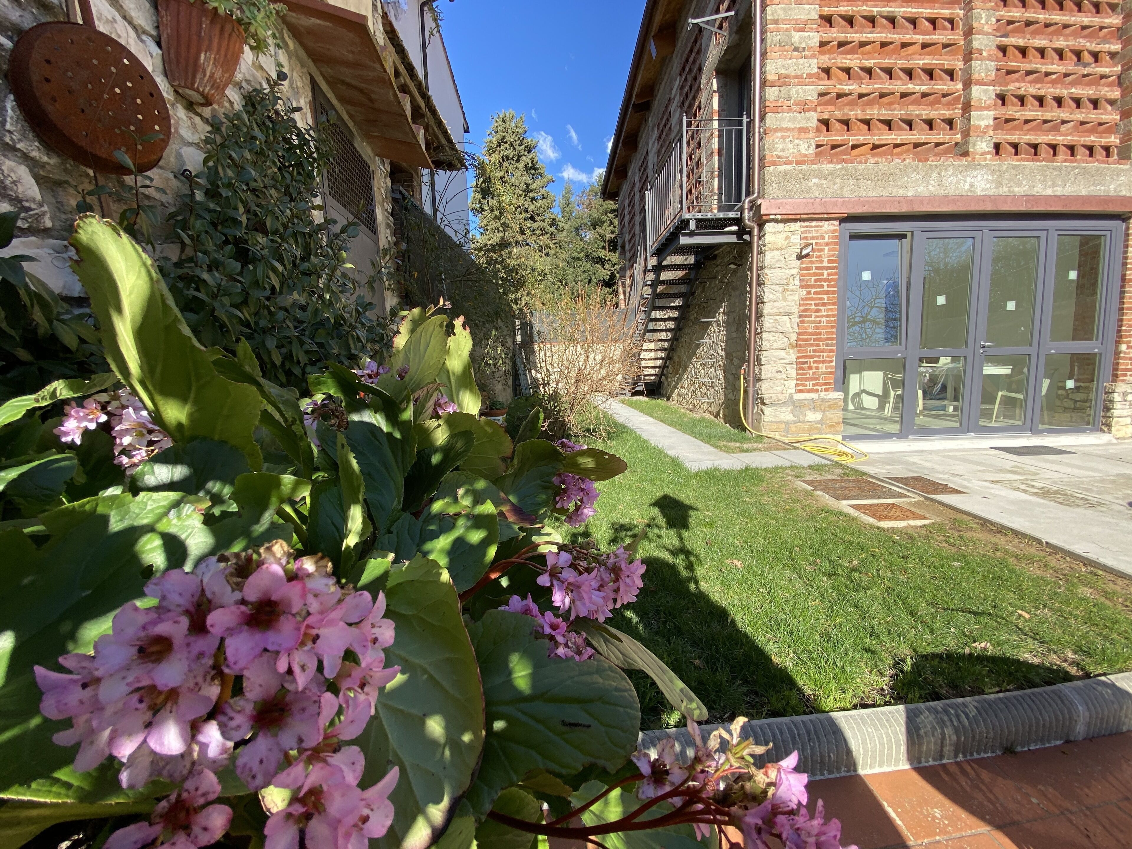 Ein Garten mit rosa Blumen und ein Backsteinhaus mit Glastür.