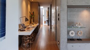 A modern interior with a wooden floor, a desk with a lamp, a vase with flowers, and a display shelf with decorative items. - Leceb Sesoko Villa (Motobu)