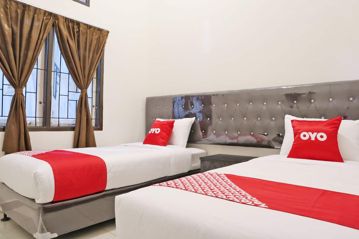 A hotel room with two beds, each with a red and white bedspread and pillows, a tufted headboard, and a window with curtains.