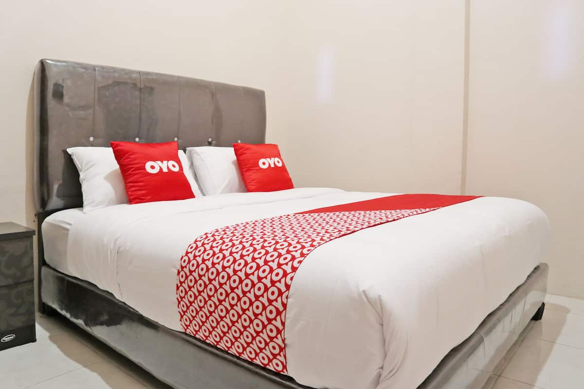 A bed with a white and red patterned bedspread, two red pillows with the text "OYO", and a grey headboard.