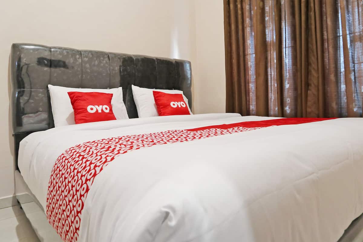 A neatly made bed with white and red bedding, two pillows with 'OYO' branding, and a dark headboard.