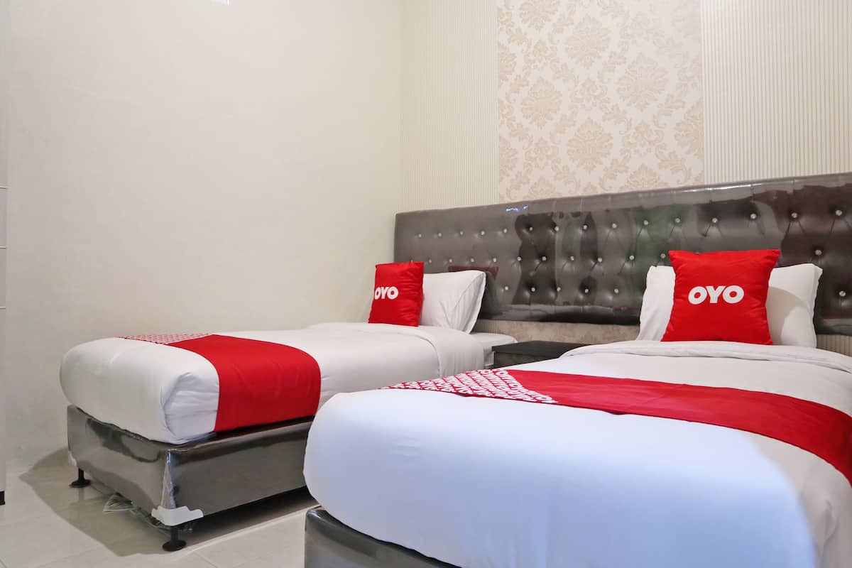 A hotel room with two beds, each with white and red bedding and pillows with 'OYO' branding.