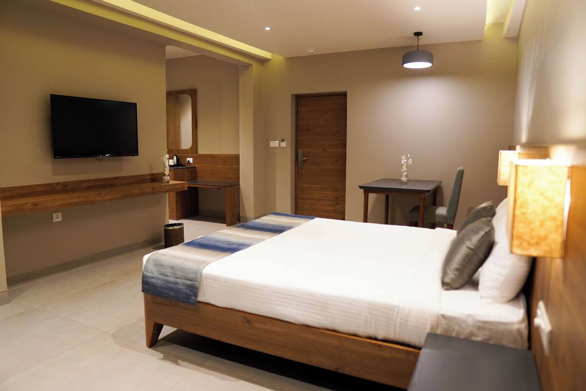 A hotel room with a bed, a TV mounted on the wall, a small table, and a chair.