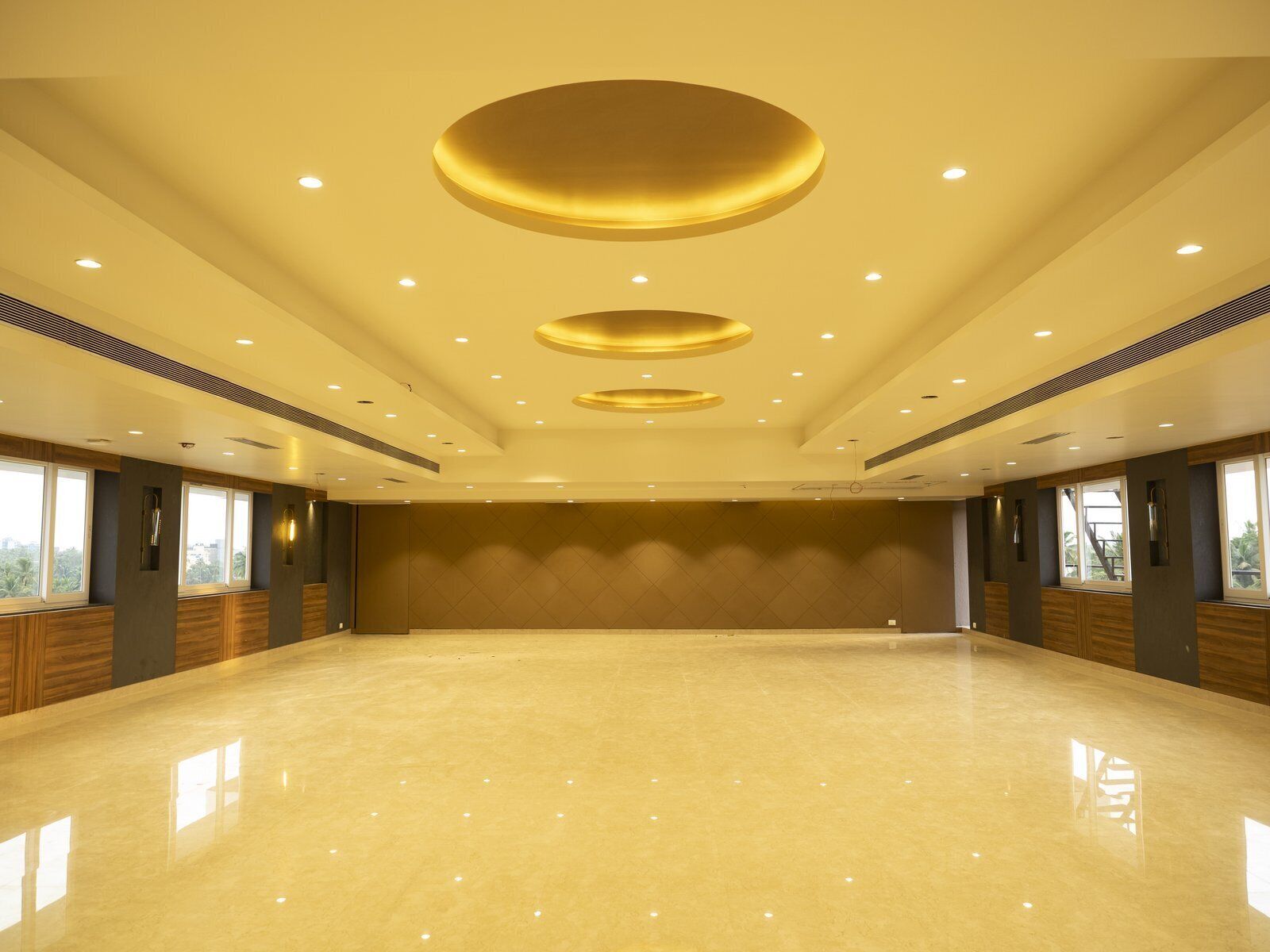 Una habitación amplia y luminosa, con piso pulido, ventanas grandes y un alto techo con lámparas de techo circulares.