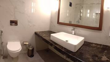 A bathroom with a white toilet, a rectangular sink with a marble countertop, a mirror with a wooden frame, and a shower area.