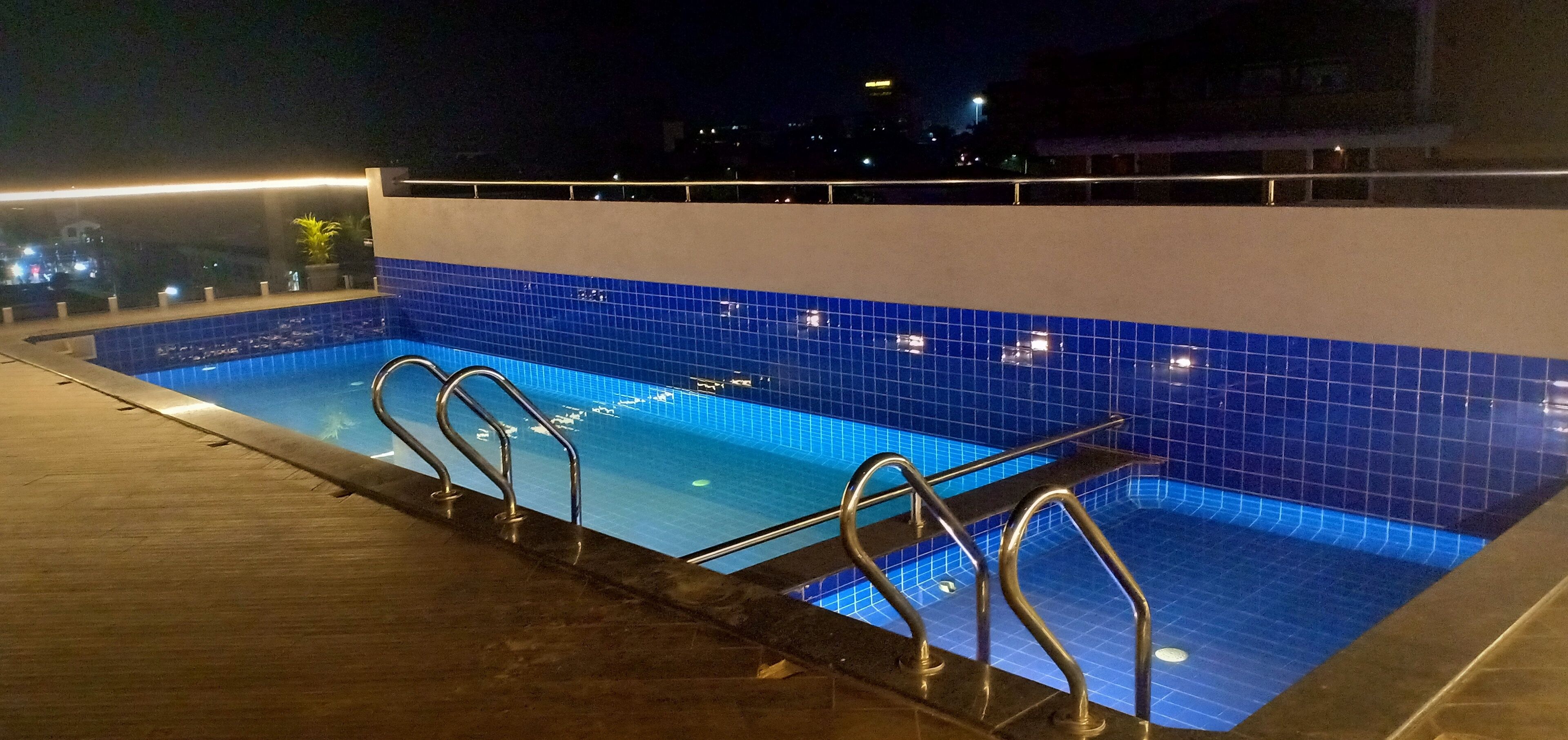 A swimming pool with blue tiles and metal railings, surrounded by a wooden deck.