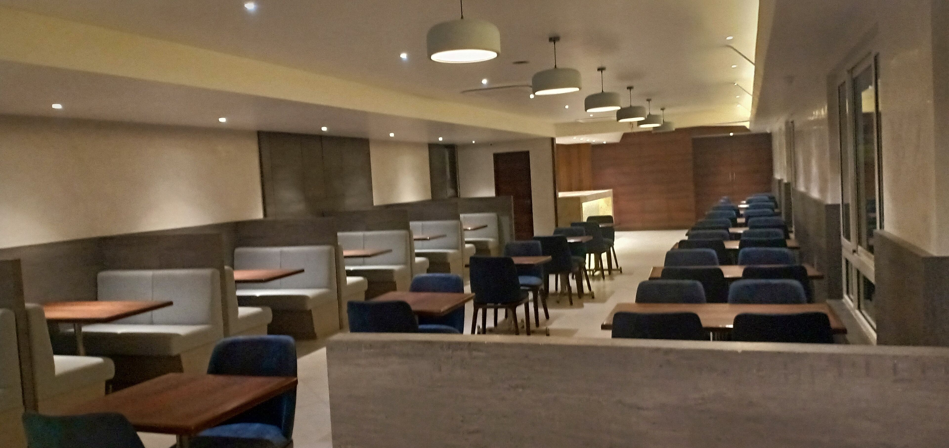 Uma sala de conferências moderna com fileiras de mesas e cadeiras, uma área de palco e uma janela grande.
