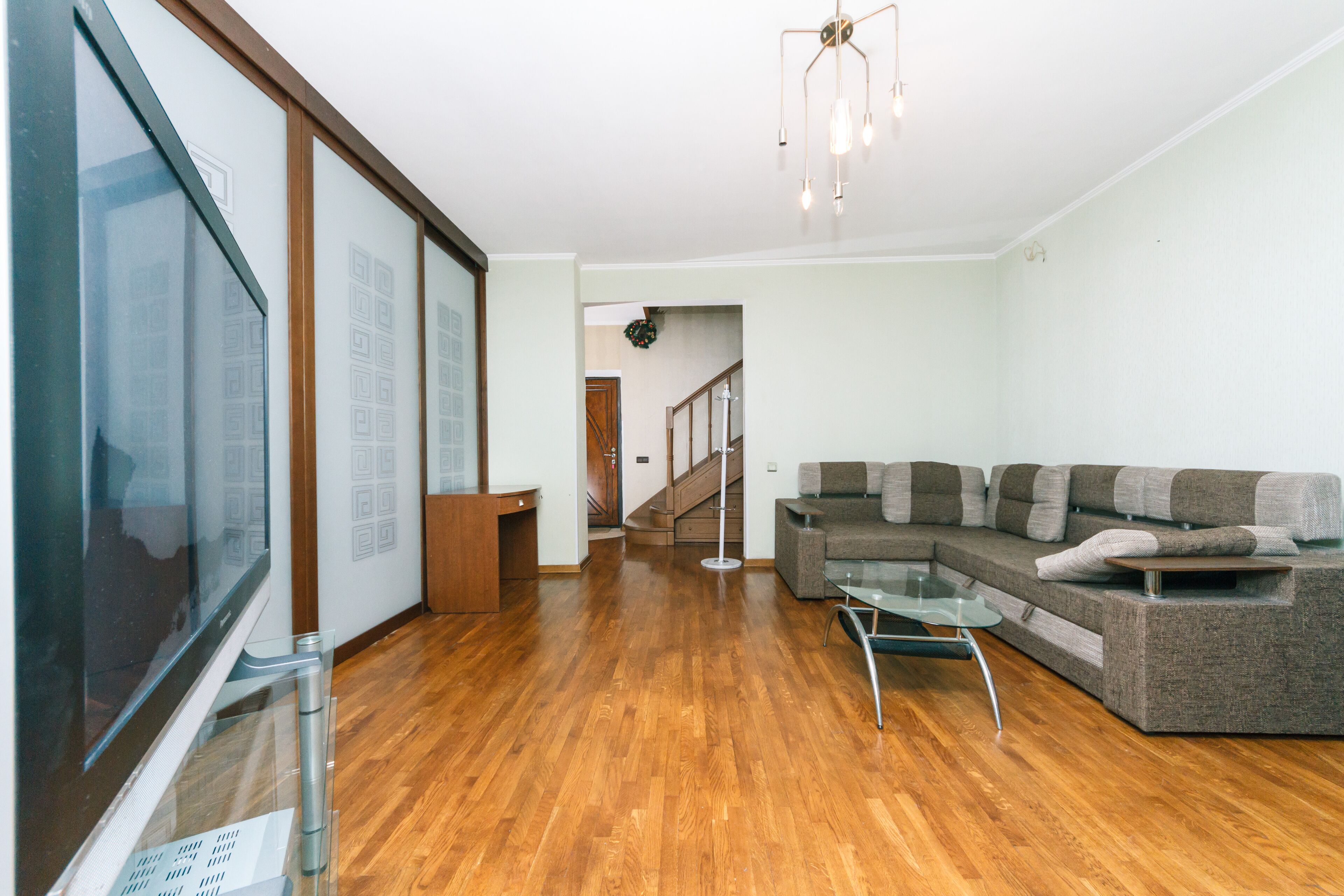 Un salón amplio con un televisor de pantalla plana grande, un sofá modular y una mesa de centro de vidrio.