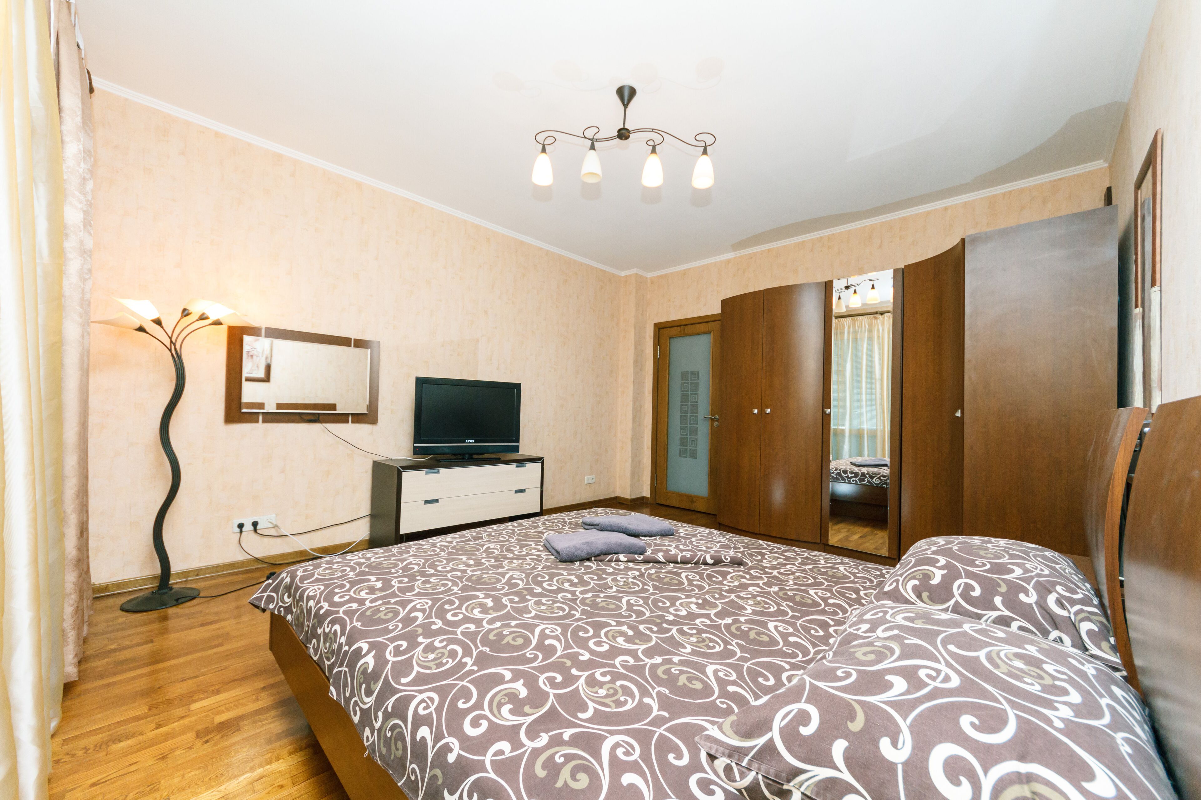 Een slaapkamer met een bed, een televisie, een kledingkast en een spiegel.