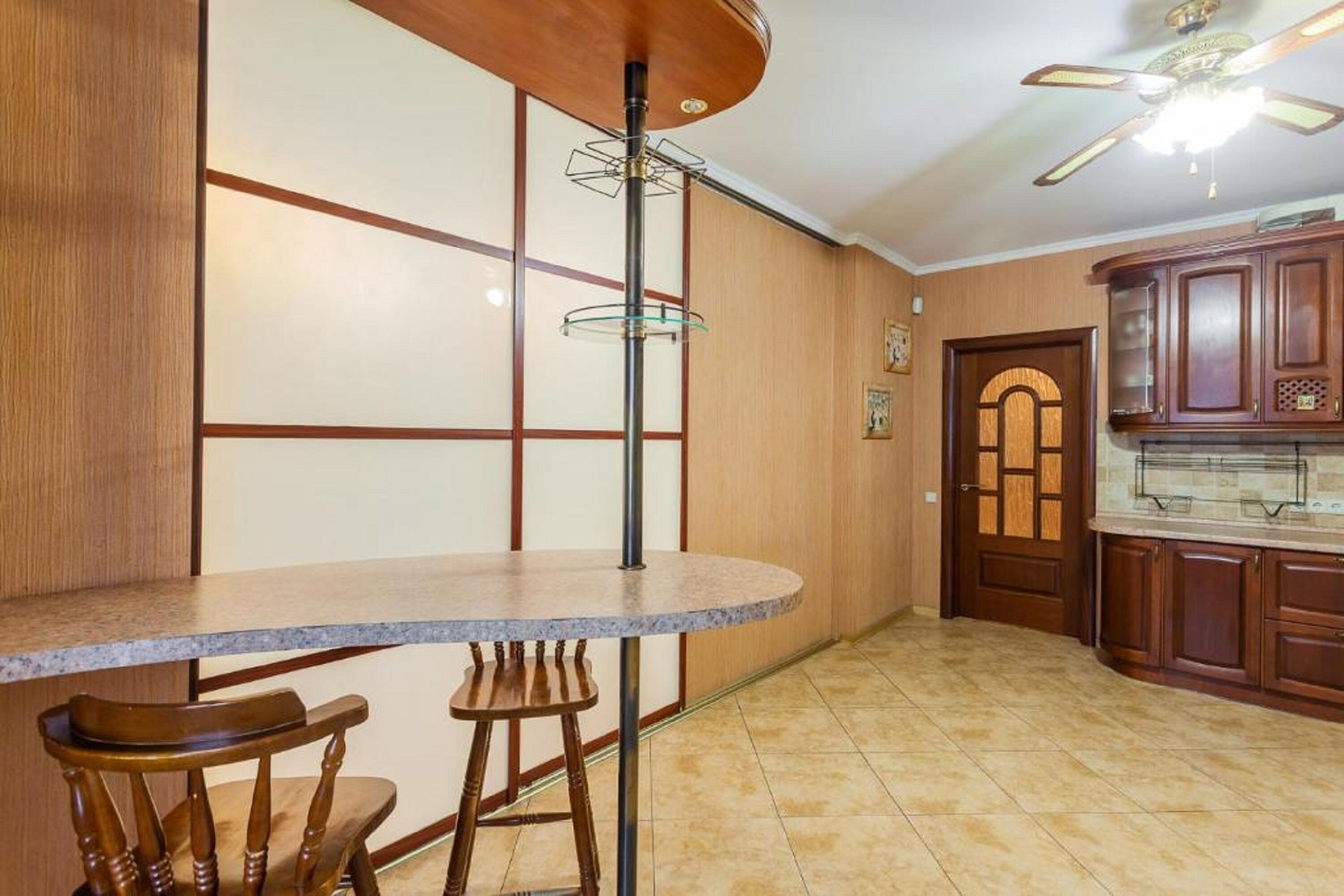 Uma cozinha com balcão, banquetas, armários de madeira e um ventilador de teto.