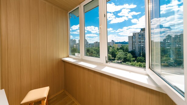 A room with wooden paneling, a window with a view of buildings and trees, and a small stool. - Apartment on Cheliabinska 19 (Kyiv)