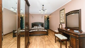 A bedroom with a wooden bed, a dresser, a bench, a mirror, and a chandelier. - Apartment on Cheliabinska 19 (Kyiv)