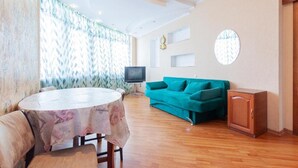 A living room with a round table, teal sofa, and a small cabinet. - Comfortable apartment on the left bank (Kyiv)
