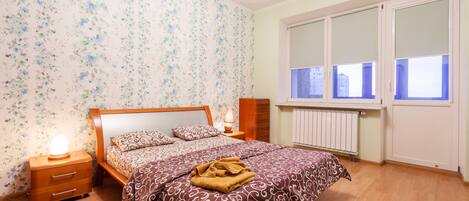 A bedroom with a wooden bed, floral wallpaper, a radiator, and a window with blinds.