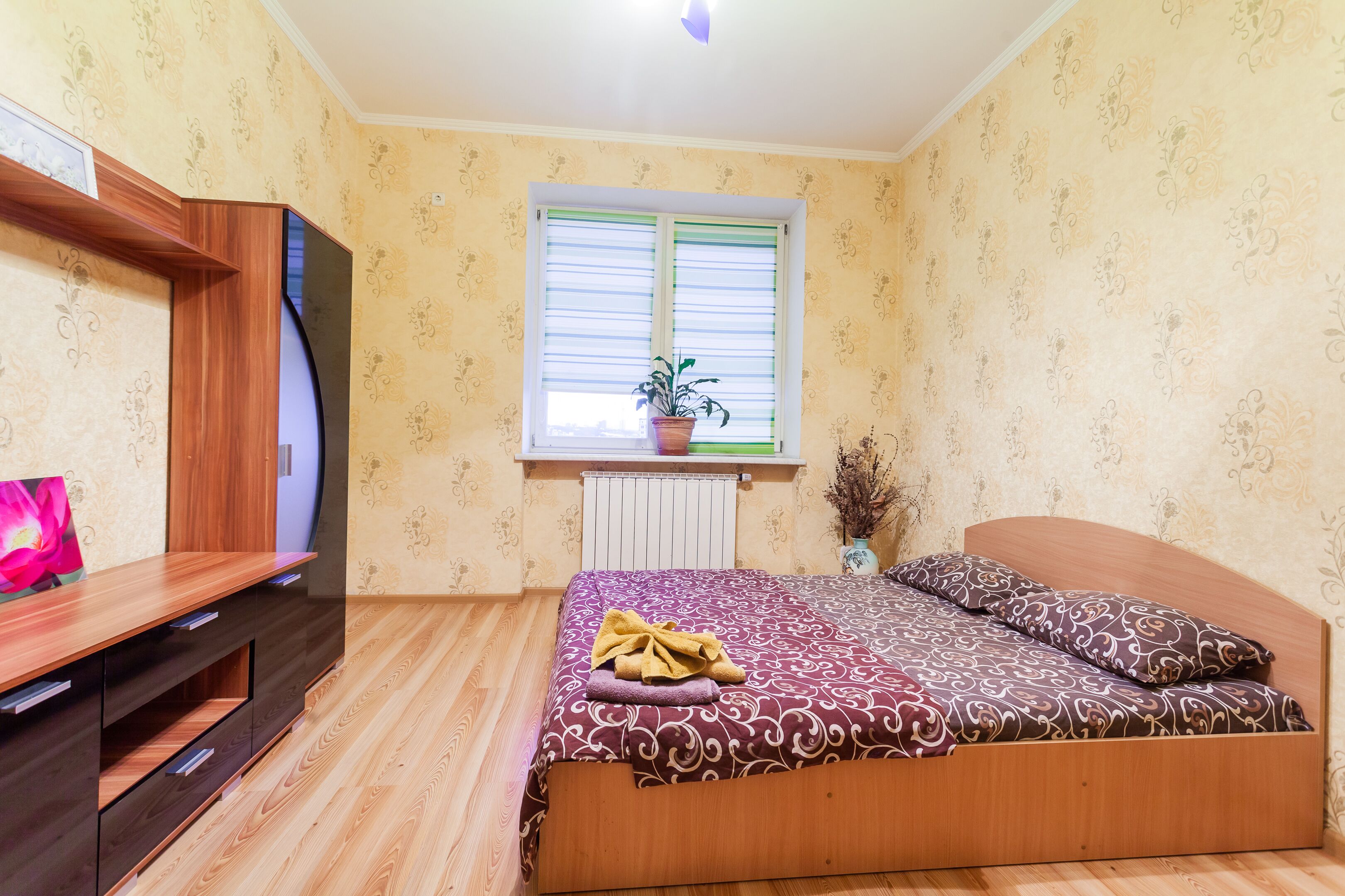Une chambre à coucher avec un lit, une commode en bois et une fenêtre avec des stores.