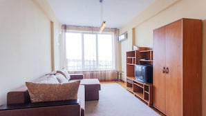 Sala de estar com sofá, televisão, armário de madeira e uma janela grande.