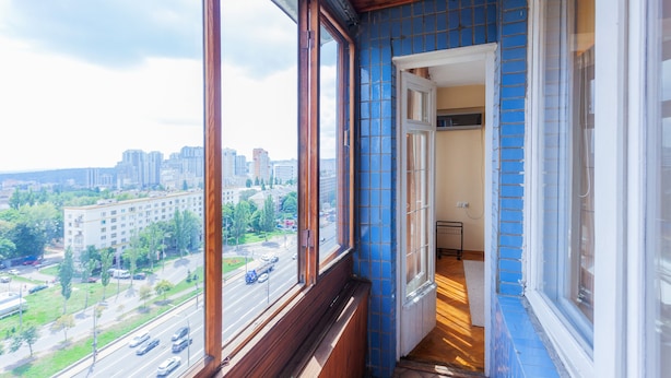 Quarto com uma grande janela com vista para a paisagem urbana, teto de madeira e parede com azulejos azuis.