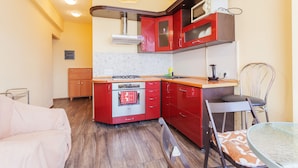 Cozinha compacta com armários vermelhos, forno embutido e micro-ondas. Possui um espaço de jantar com mesa e cadeiras.