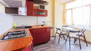 Cozinha compacta com fogão a gás, micro-ondas e armários vermelhos. Há uma mesa de jantar com cadeiras e uma janela com cortinas.
