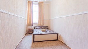 Un dormitorio con cama, mesita de noche, radiador y ventana con cortinas.
