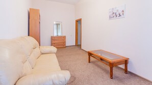 Una habitación con un sofá de cuero color beige, una mesa de madera, un aparador de madera y una puerta que da a otra estancia.