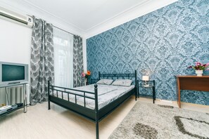 A bedroom with a bed, a bedside table, a lamp, a TV, and a radiator.