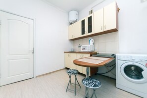 A compact kitchen with a washing machine, a coffee maker, and two stools.