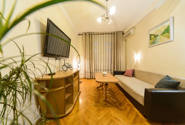 A cozy living room with a sofa, a coffee table, a TV mounted on the wall, and a bicycle.