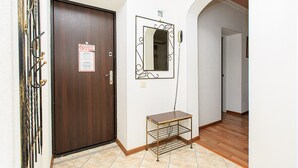 Un pasillo con una puerta de madera, un espejo de estructura metálica y una pequeña estantería de metal.