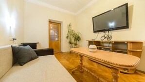 Una sala de estar con un sofá, una mesa de centro de madera, un televisor montado en la pared, una bicicleta y una puerta con paneles de vidrio esmerilado.