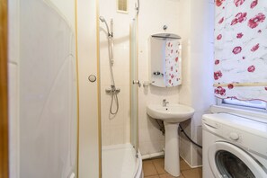 A bathroom with a shower, sink, and washing machine.
