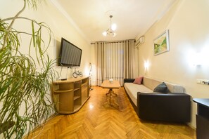 A living room with a wooden floor, a sofa, a TV, a table, and a plant.