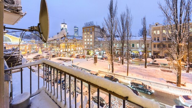 Escena urbana nevada con edificios, un hotel visible y una barandilla cubierta de nieve.