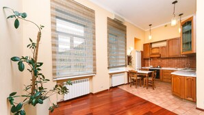 A modern kitchen with wooden cabinets, a dining area, and large windows with blinds. - Apartment near Olympic Stadium (Kyiv)