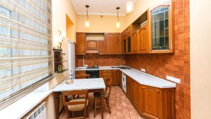 A compact kitchen with wooden cabinets, a built-in oven, a sink, and a dining area with a table and chairs. - Apartment near Olympic Stadium (Kyiv)