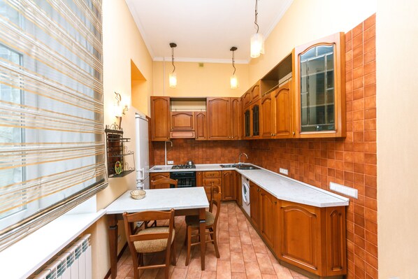 A compact kitchen with wooden cabinets, a built-in oven, a sink, and a dining area with a table and chairs.